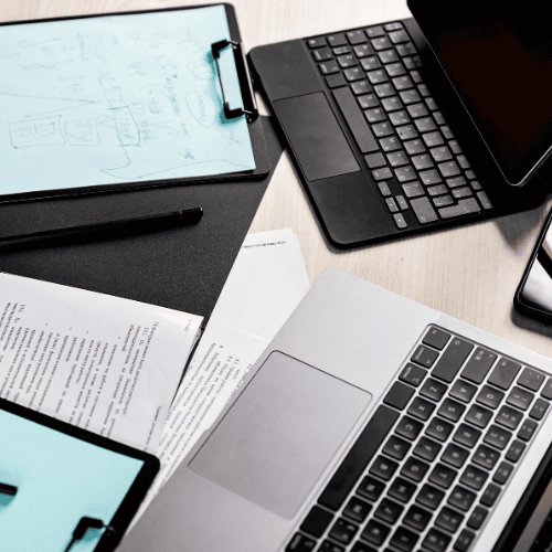Workspace setup for digital strategy planning, featuring a laptop, tablet, documents, and handwritten notes on a clipboard.
